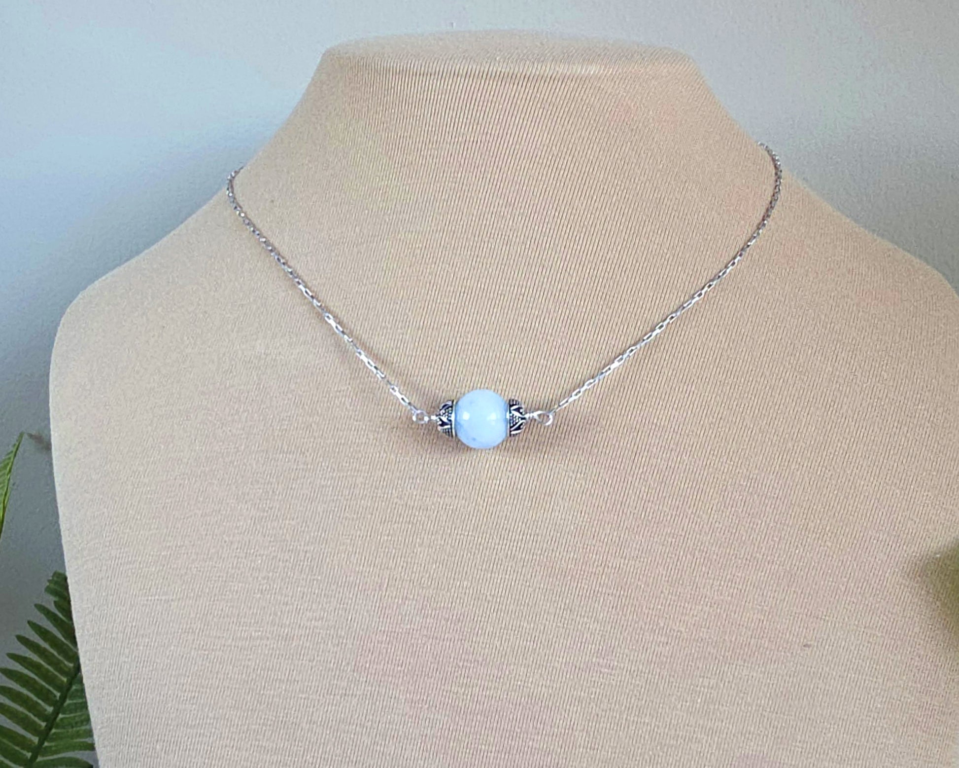 Aquamarine Necklace with one large single round blue Aquamarine stone with silver caps on beige background display