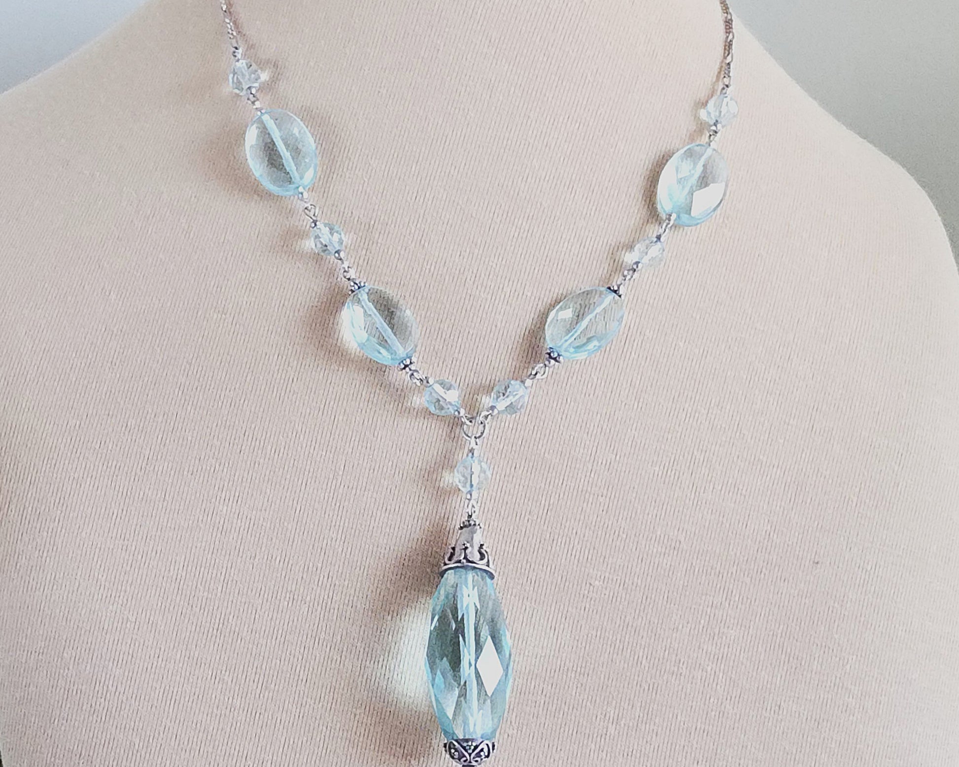 Sparkly pale aqua blue translucent synthetic Aquamarine stones and Sterling Silver beads and chain on beige background