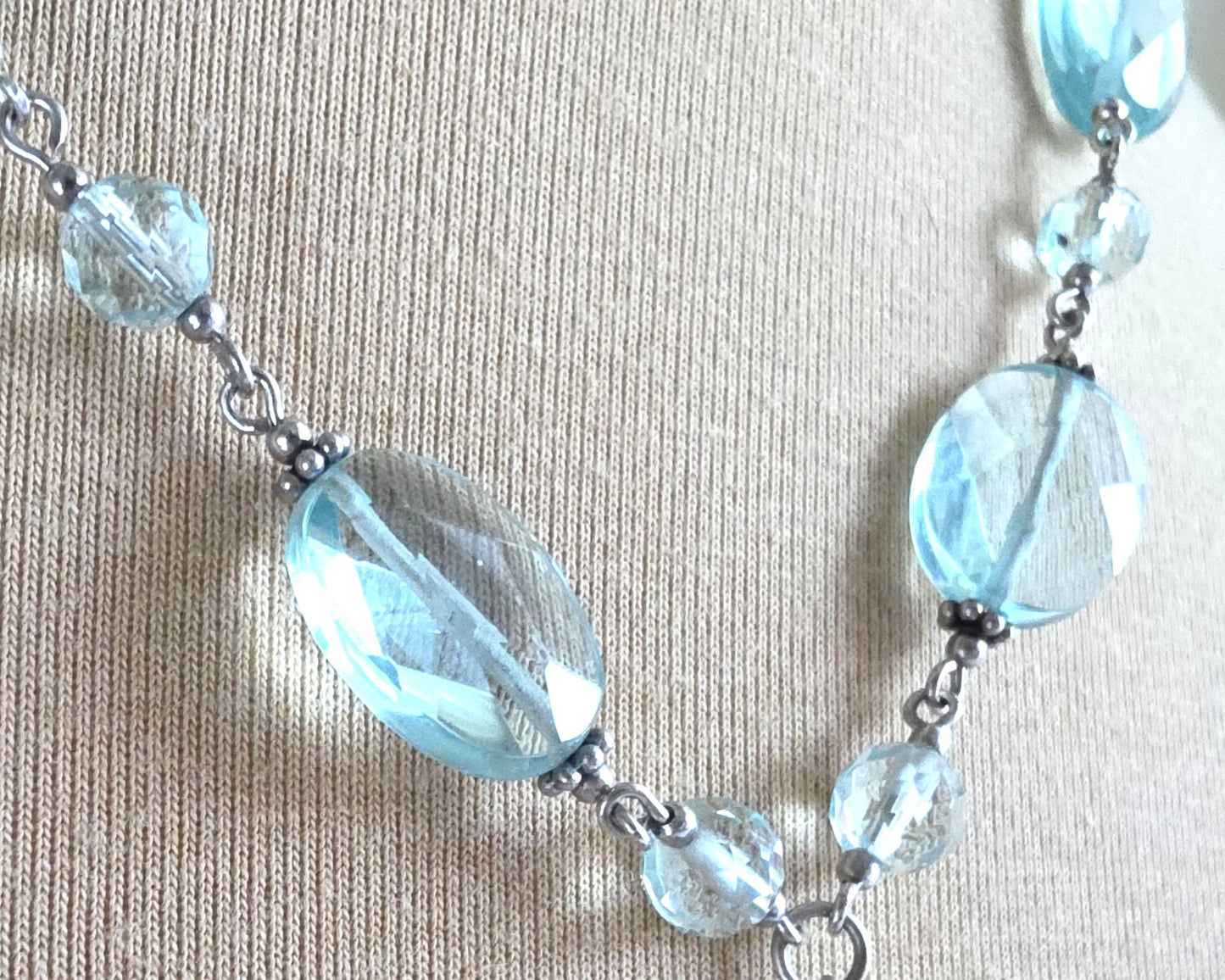 Sparkly pale aqua blue translucent synthetic Aquamarine stones and Sterling Silver beads and chain on beige background 