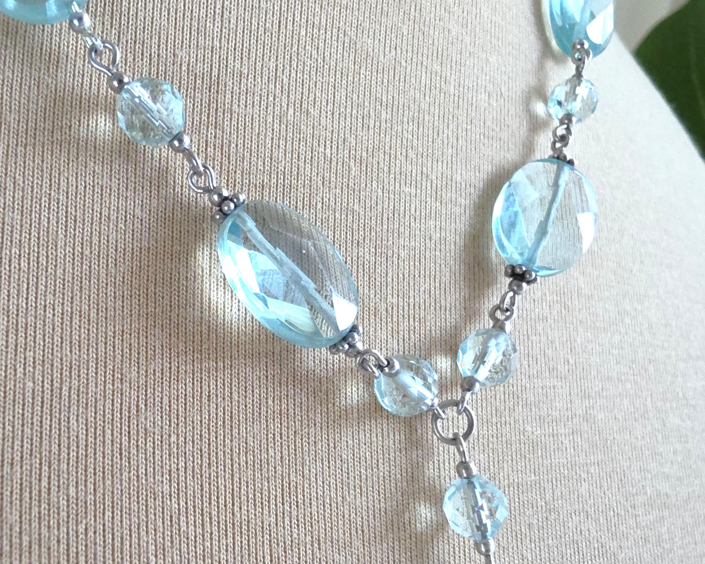 Sparkly pale aqua blue translucent synthetic Aquamarine stones and Sterling Silver beads and chain on beige background 