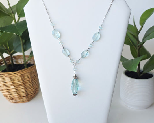 Art Deco style Aquamarine necklace made with large faceted, sparkly pale aqua blue translucent synthetic Aquamarine stones and Sterling Silver beads and chain on white background and plants 