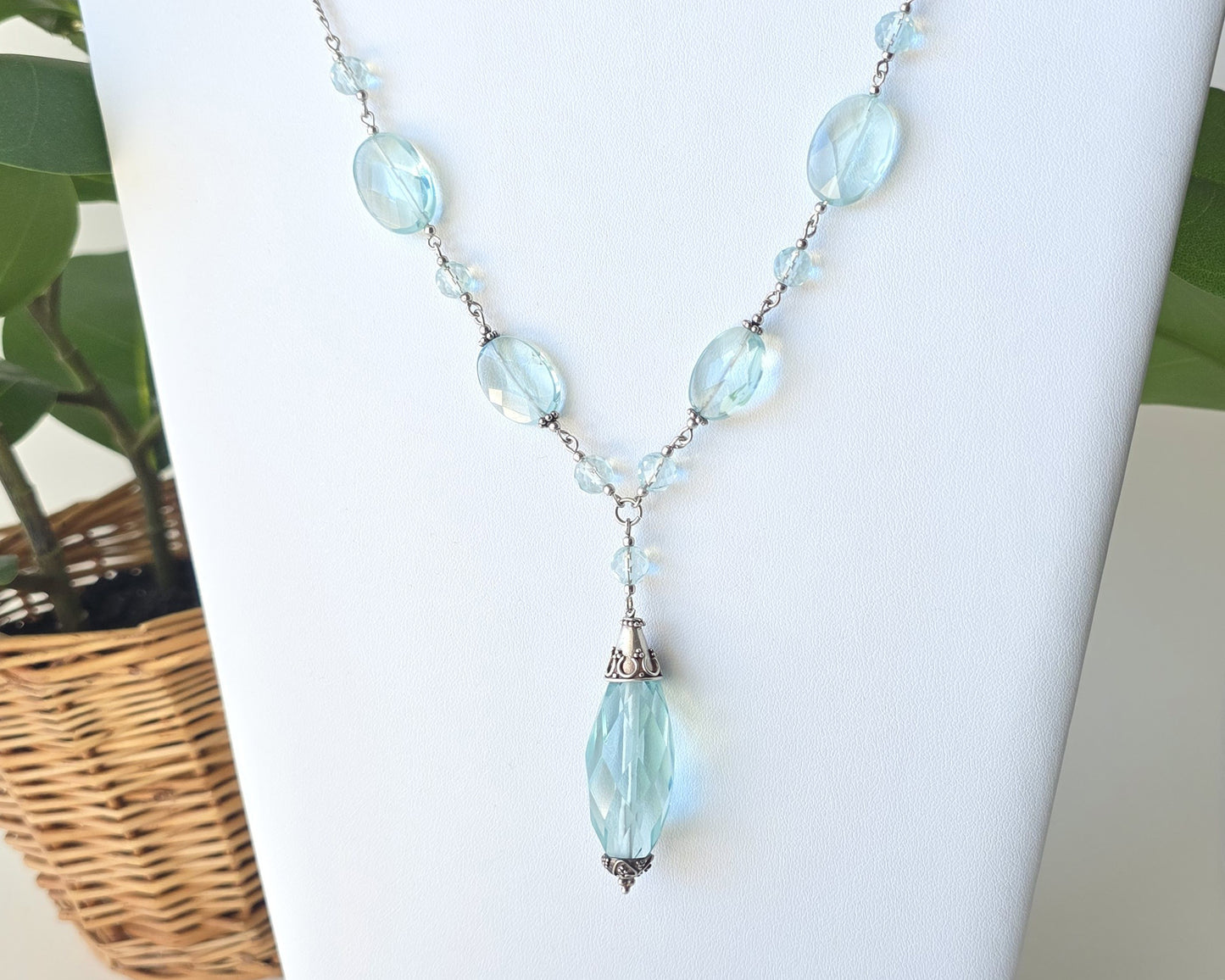 Art Deco style Aquamarine necklace made with large faceted, sparkly pale aqua blue translucent synthetic Aquamarine stones and Sterling Silver beads and chain on white background and plants 