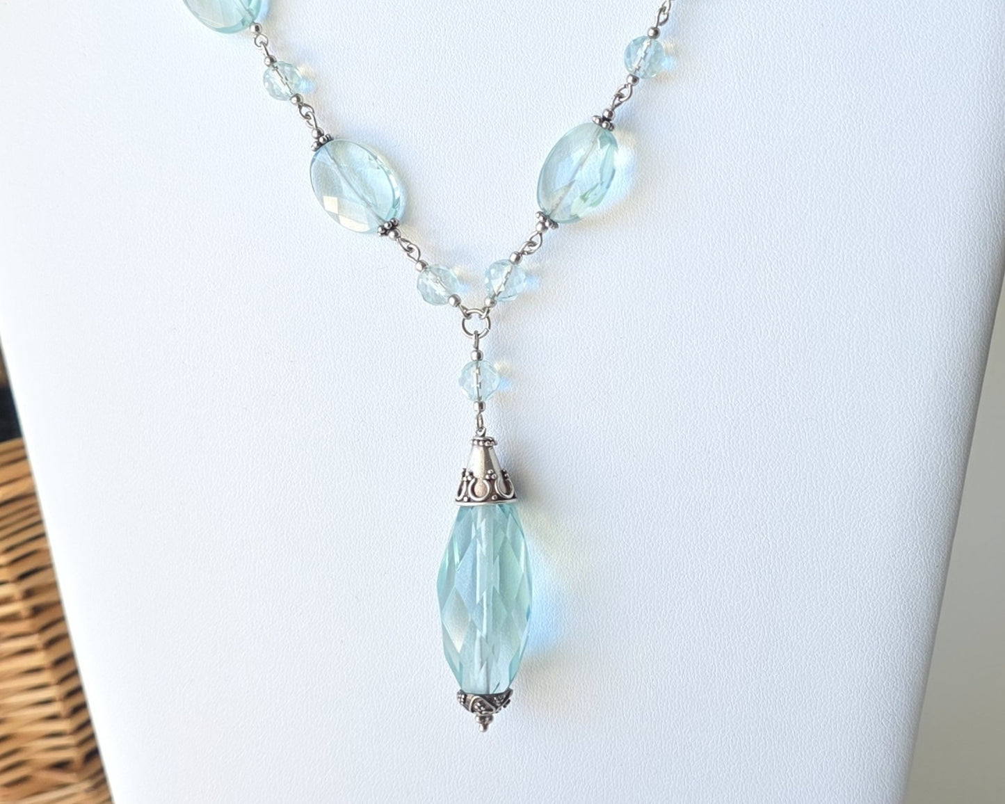 Art Deco style Aquamarine necklace made with large faceted, sparkly pale aqua blue translucent synthetic Aquamarine stones and Sterling Silver beads and chain on white background and plants 