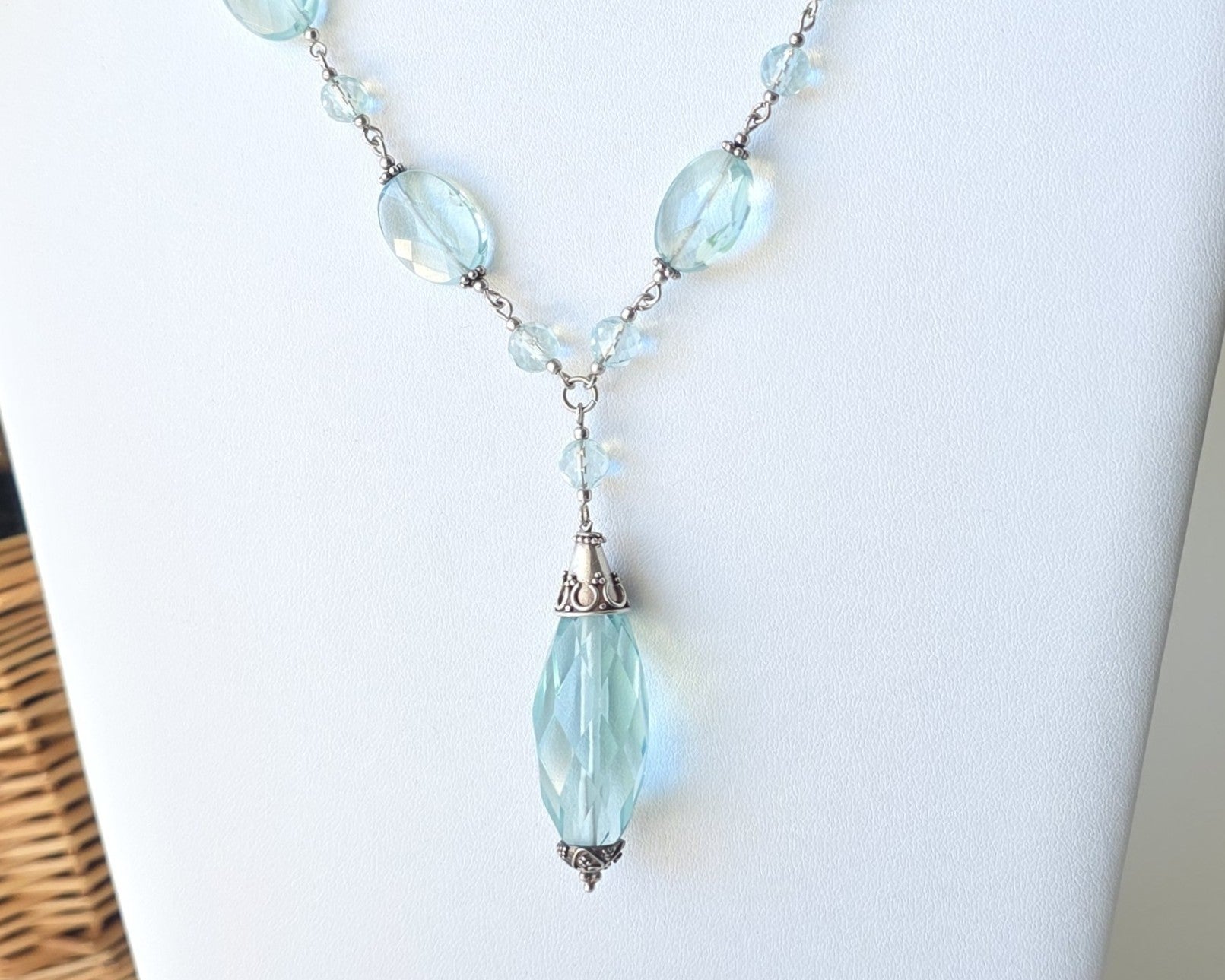 Art Deco style Aquamarine necklace made with large faceted, sparkly pale aqua blue translucent synthetic Aquamarine stones and Sterling Silver beads and chain on white background and plants 