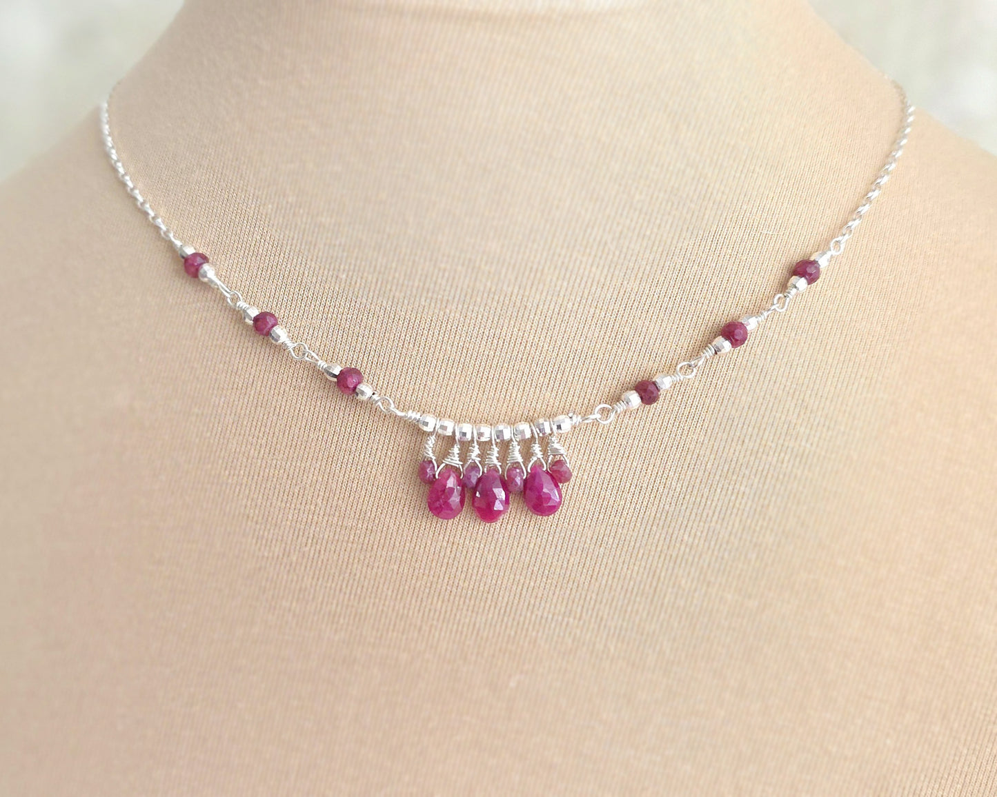 Silver and red Ruby necklace on beige display bust and lace background 