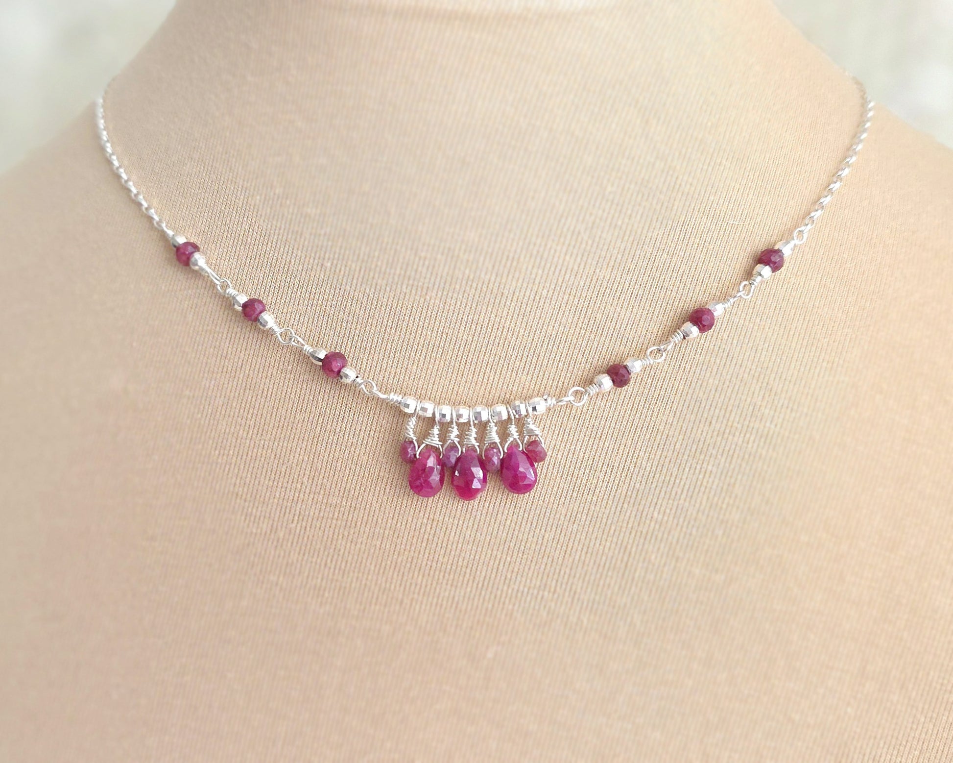 Silver and red Ruby necklace on beige display bust and lace background 
