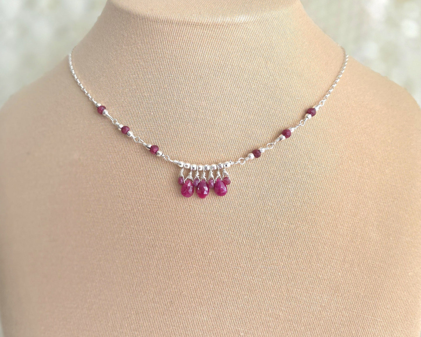 Silver and red Ruby necklace on beige display bust and lace background 