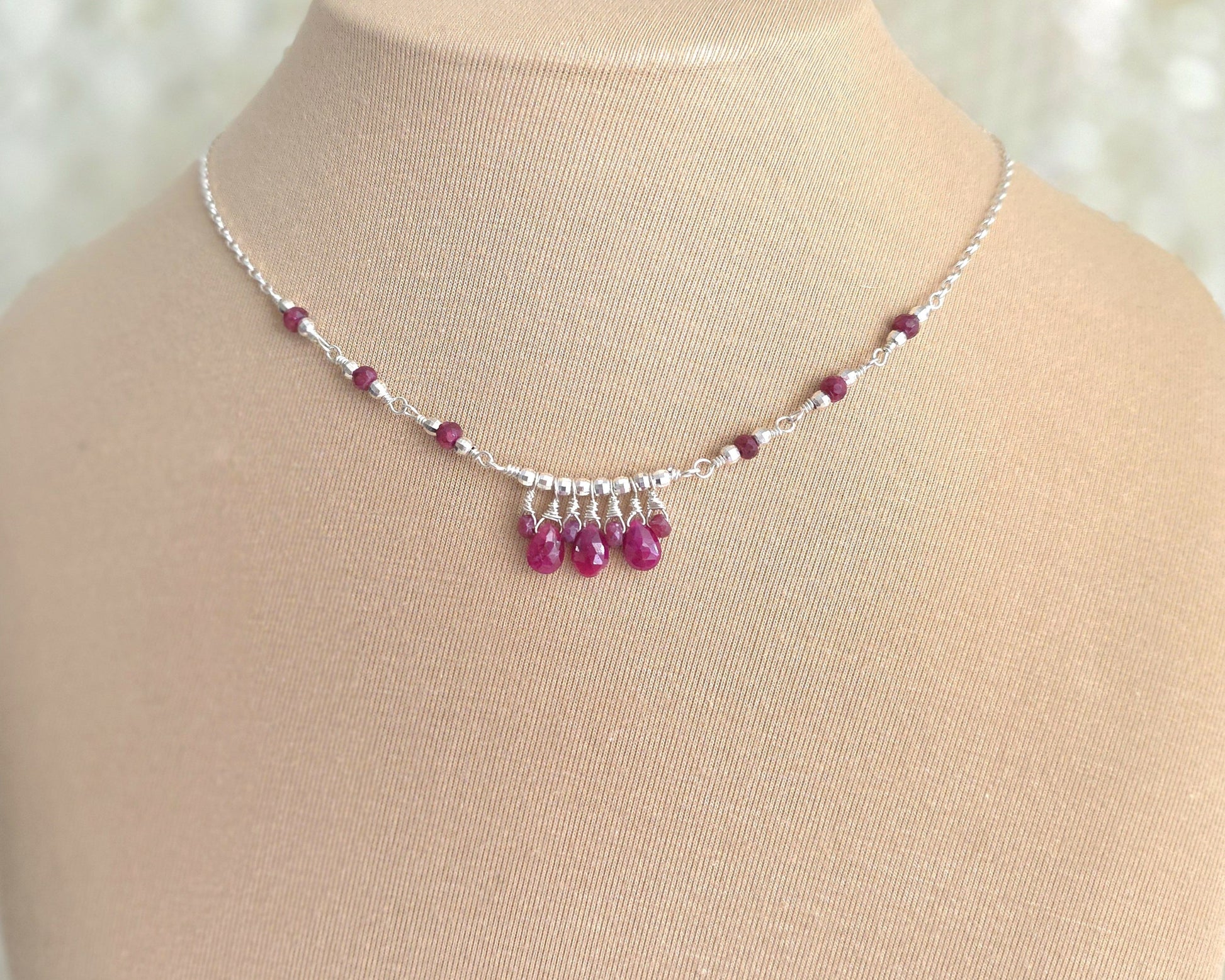 Silver and red Ruby necklace on beige display bust and lace background 