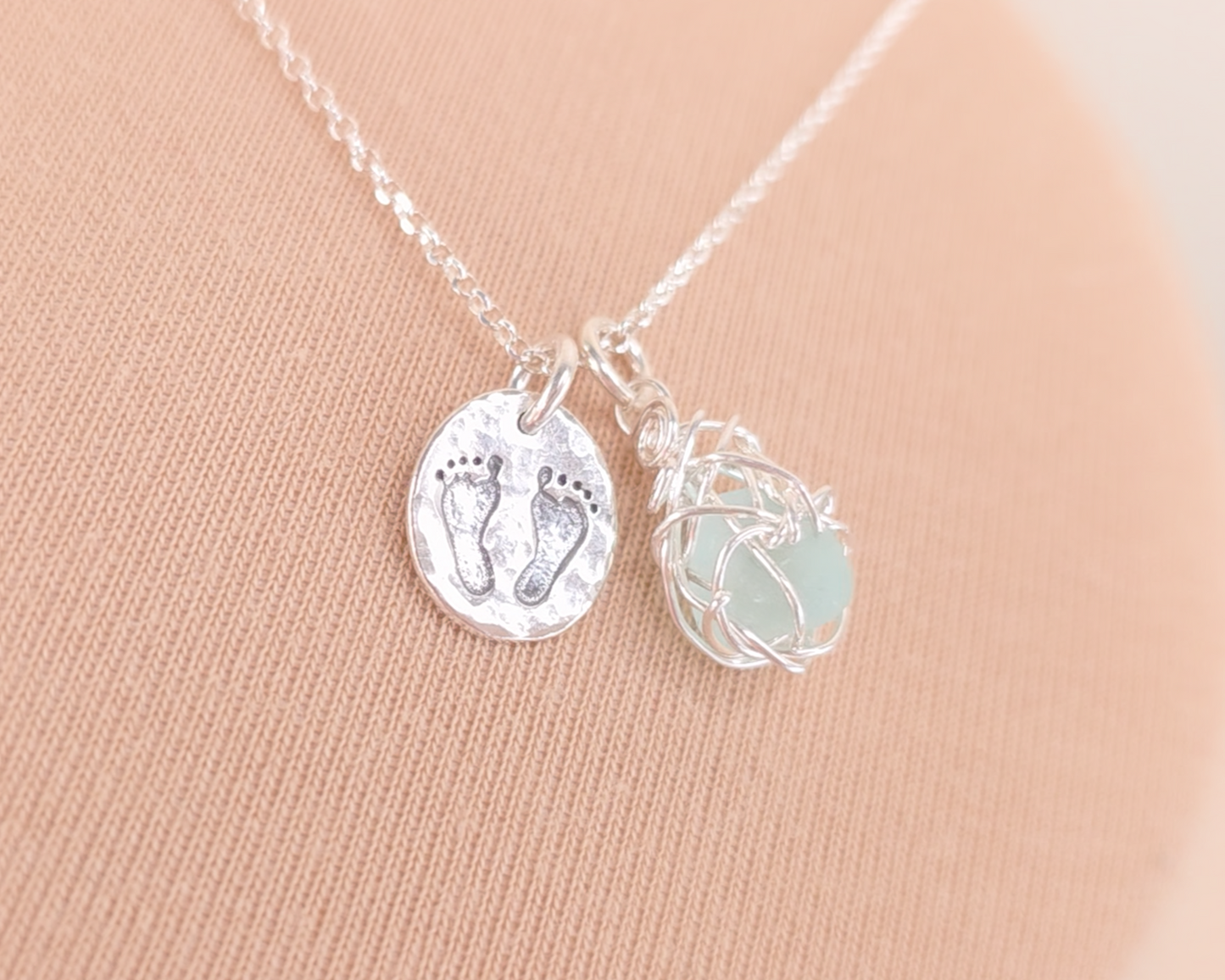 Pale Blue Sea Glass Pendant with round Silver Pendant with Footprints on Chain displayed on beige background 