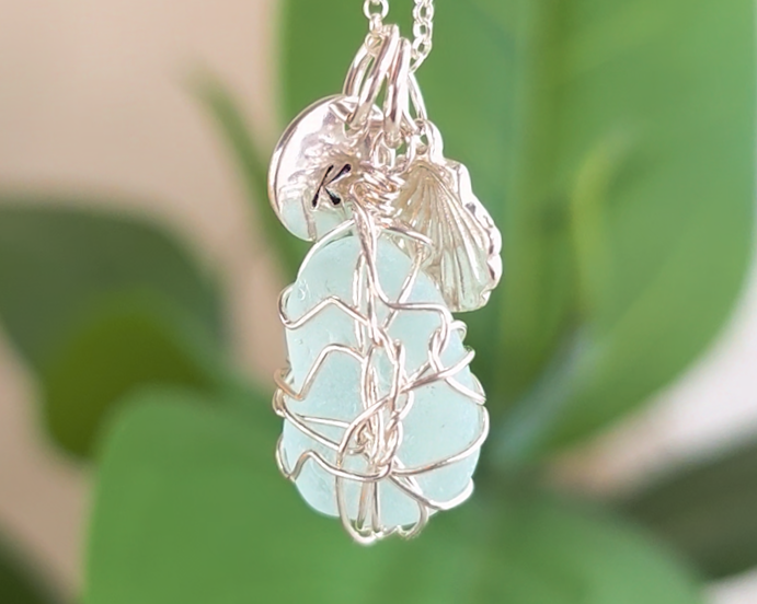 Silver Sea Glass Necklace with Aqua blue Sea Glass wire wrapped with shell & initial pendants on chain with green plants in the background 