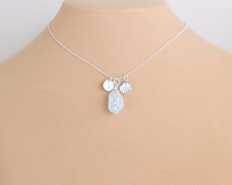Silver Sea Glass Necklace with Aqua blue Sea Glass wire wrapped with shell & initial pendants on chain with beige background 