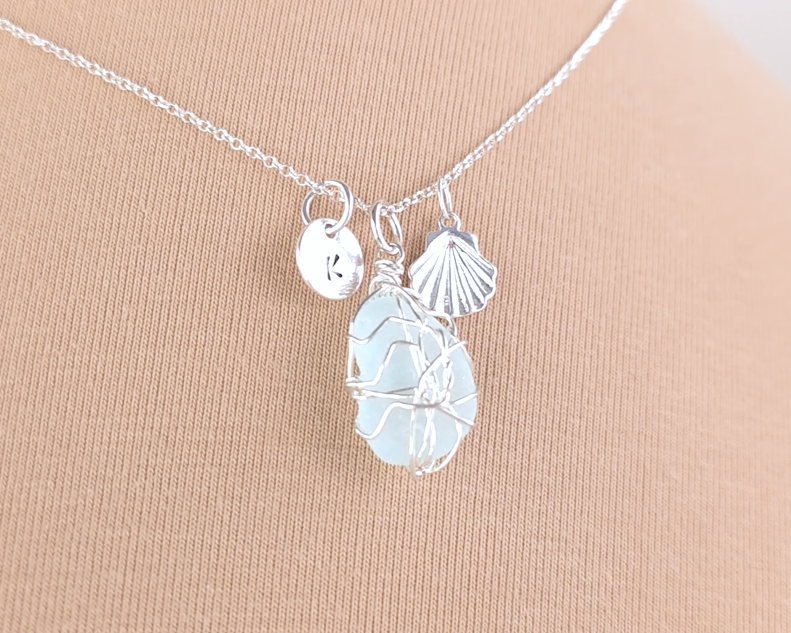 Silver Sea Glass Necklace with Aqua blue Sea Glass wire wrapped with shell & initial pendants on chain with beige background 
