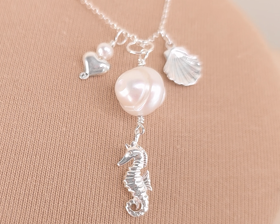 Silver Necklace with white Pearls, Silver Seahorse, Shell and Heart Pendants on chain with beige background 