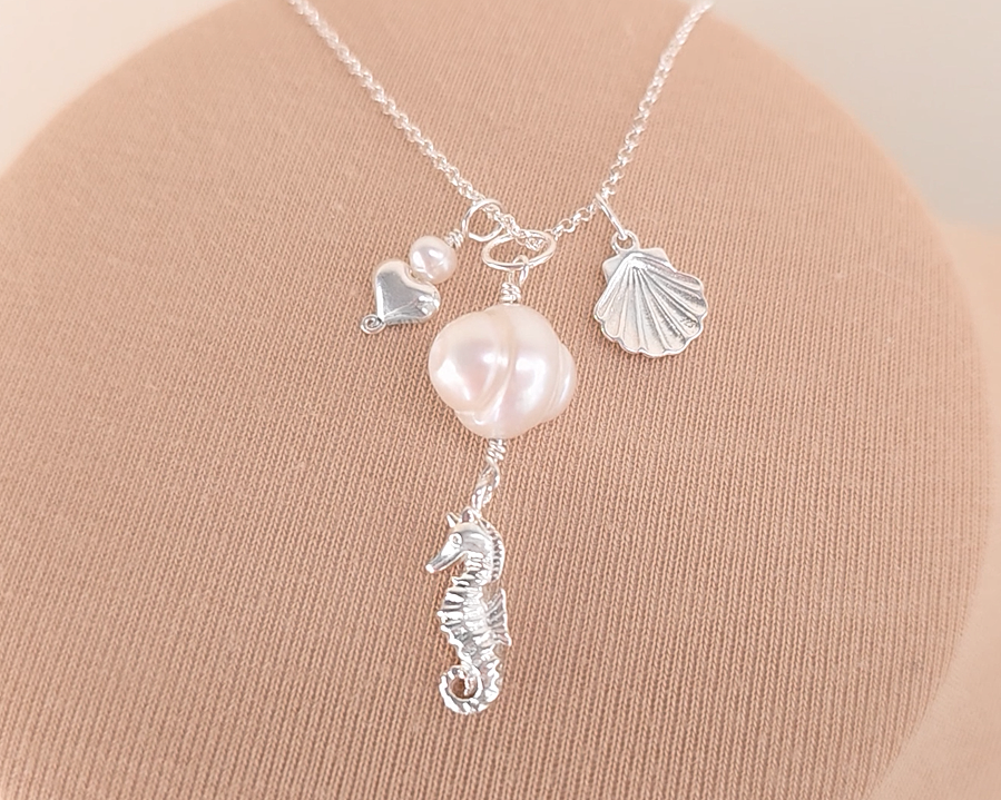 Silver Necklace with white Pearls, Silver Seahorse, Shell and Heart Pendants on chain with beige background 