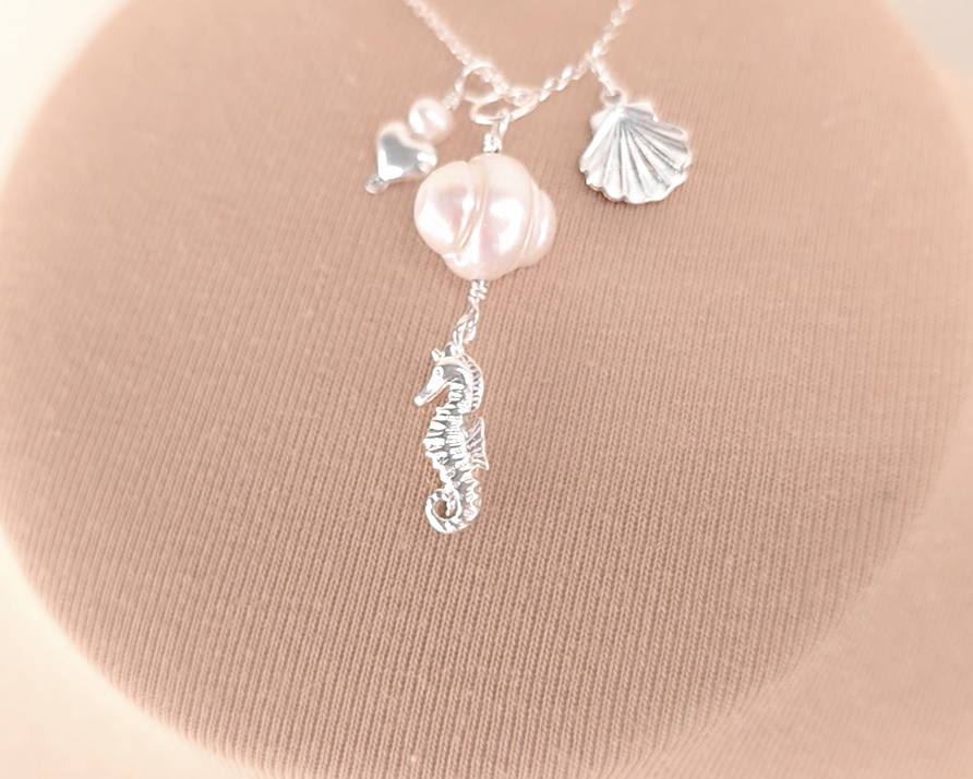 Silver Necklace with white Pearls, Silver Seahorse, Shell and Heart Pendants on chain with beige background