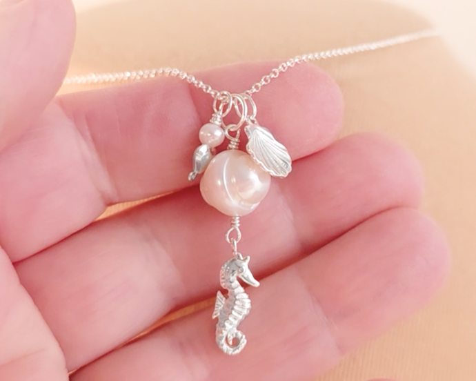 Silver Necklace with white Pearls, Silver Seahorse, Shell and Heart Pendants on chain on hand over fingers 