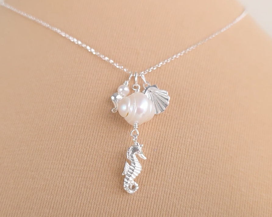 Silver Necklace with white Pearls, Silver Seahorse, Shell and Heart Pendants on chain with beige background