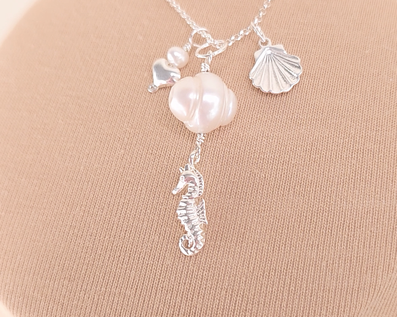Silver Necklace with white Pearls, Silver Seahorse, Shell and Heart Pendants on chain with beige background