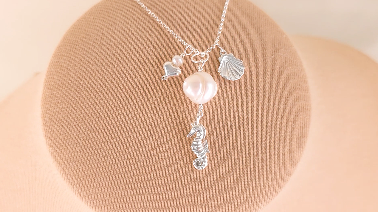 Silver Necklace with white Pearls, Silver Seahorse, Shell and Heart Pendants on chain with beige background