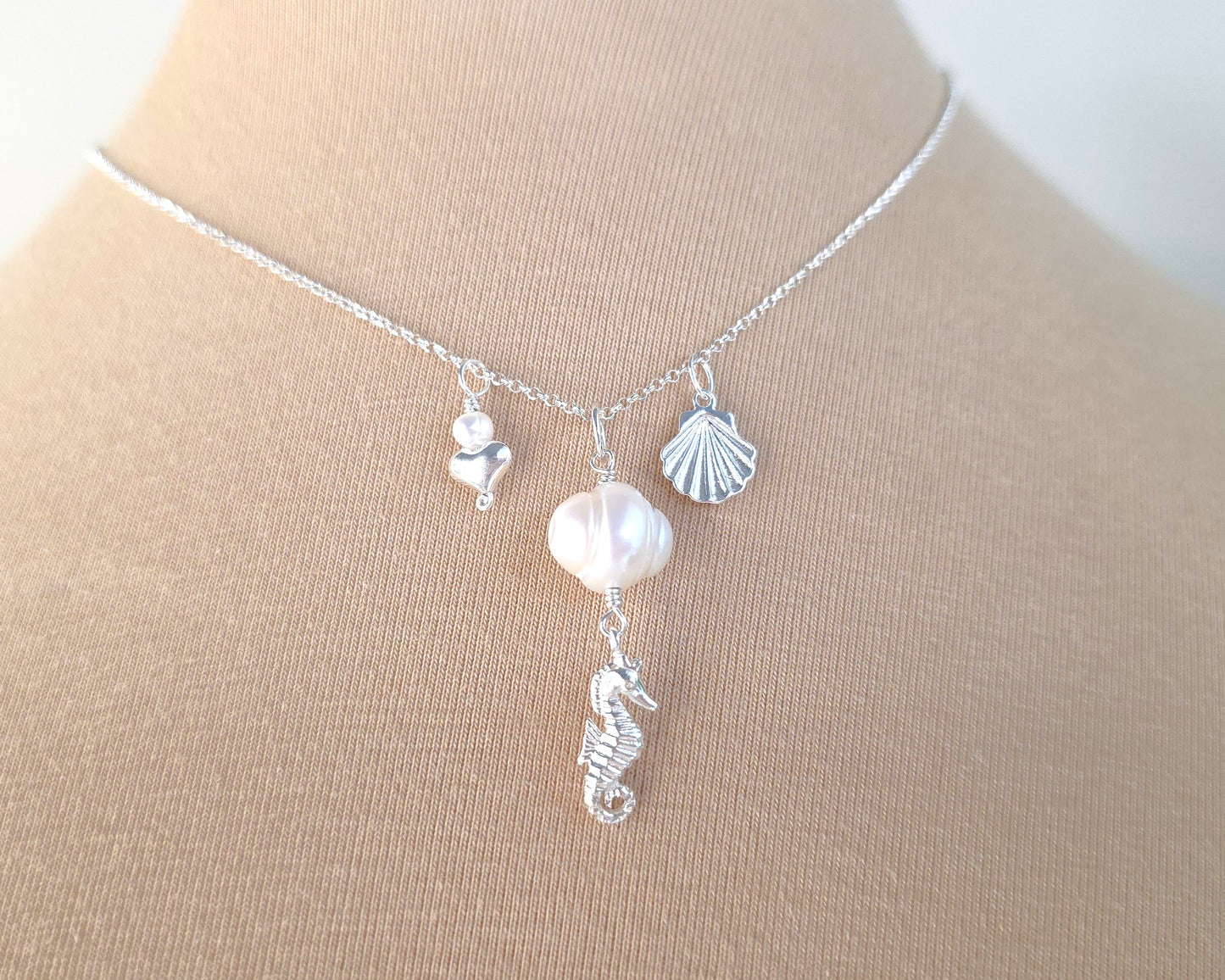 Silver Necklace with white Pearls, Silver Seahorse, Shell and Heart Pendants on chain with beige background