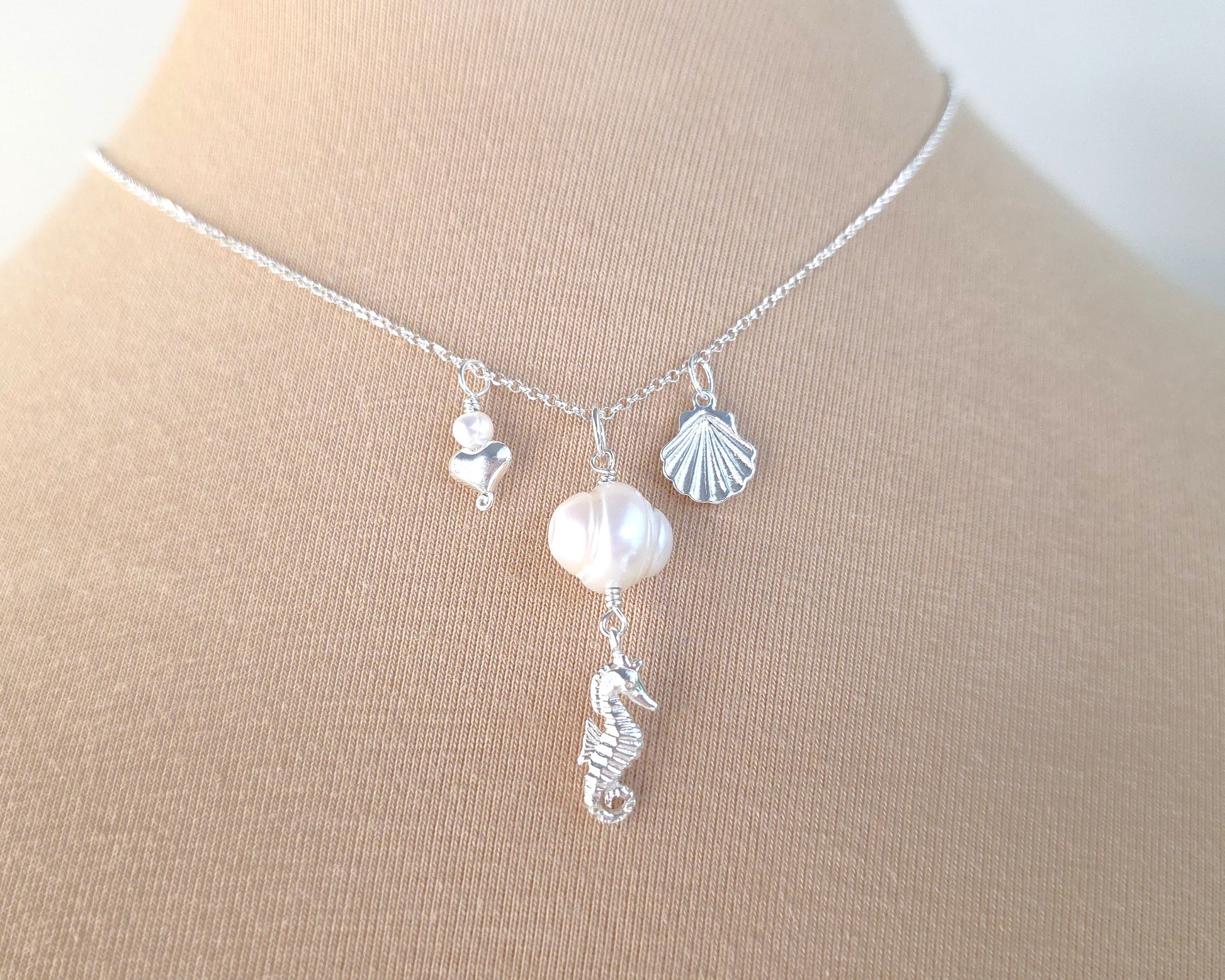 Silver Necklace with white Pearls, Silver Seahorse, Shell and Heart Pendants on chain with beige background