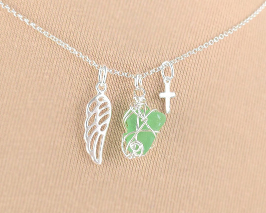 Silver necklace with green sea glass wire wrapped pendant with a silver wing and small cross on chain with beige background