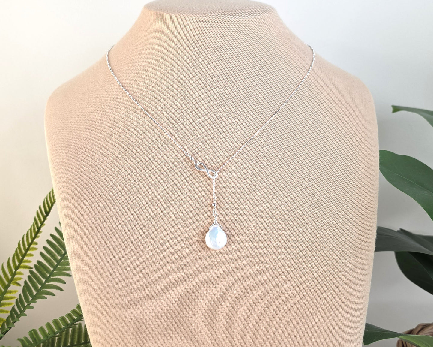 Large Pearl Drop Sterling Silver Infinity Lariat Necklace on beige display bust with plants in background 