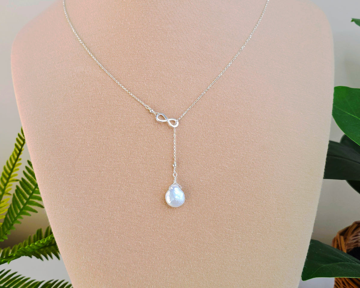 Large Pearl Drop Sterling Silver Infinity Lariat Necklace on beige display bust with plants in background 
