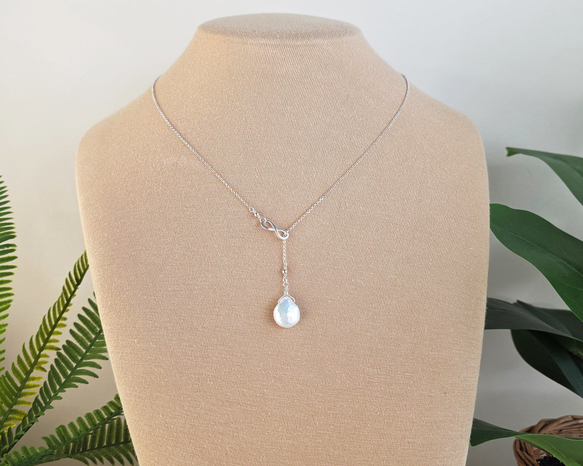 Large Pearl Drop Sterling Silver Infinity Lariat Necklace on beige display bust with plants in background 
