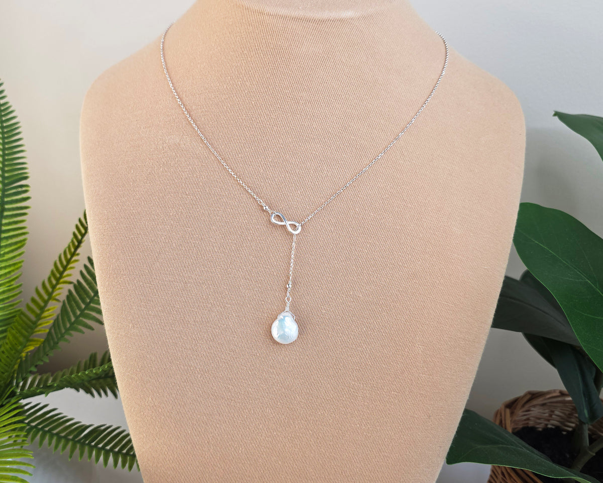 Large Pearl Drop Sterling Silver Infinity Lariat Necklace on beige display bust with plants in background 
