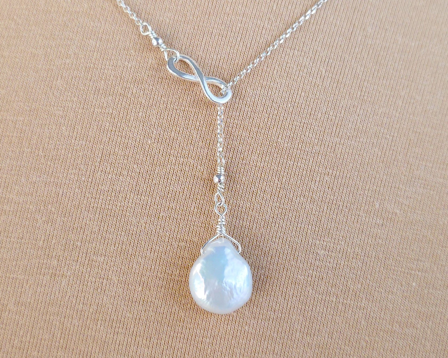 Large Pearl Drop Sterling Silver Infinity Lariat Necklace on beige display 