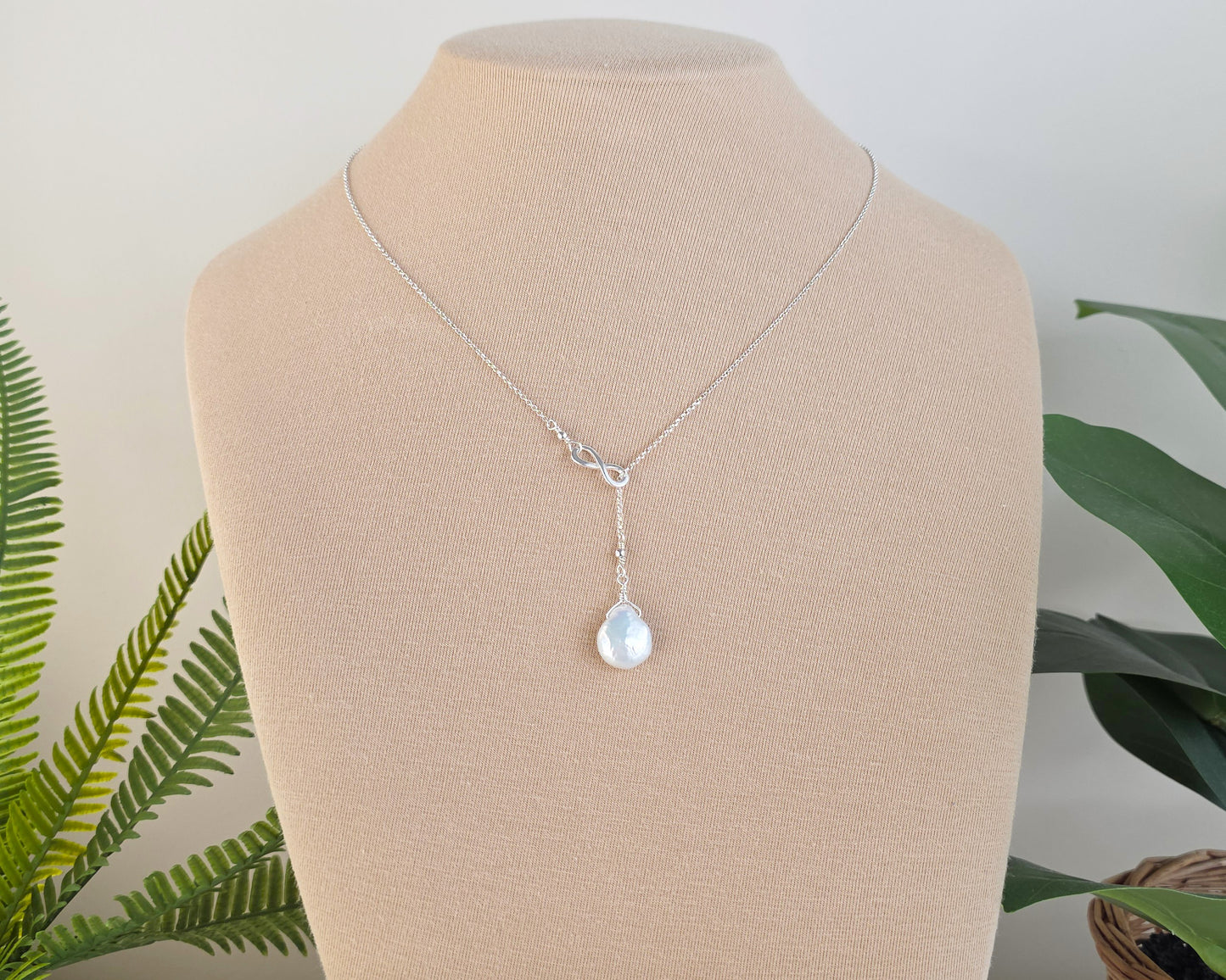 Large Pearl Drop Sterling Silver Infinity Lariat Necklace on beige display bust with plants in background 