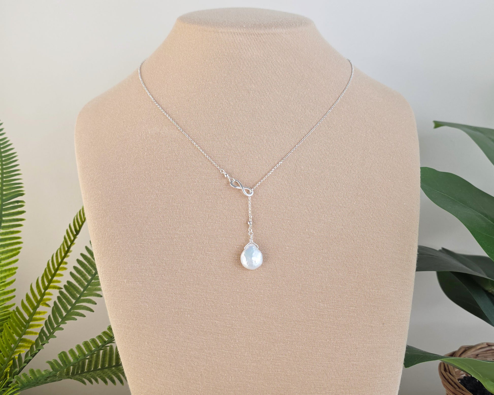 Large Pearl Drop Sterling Silver Infinity Lariat Necklace on beige display bust with plants in background 