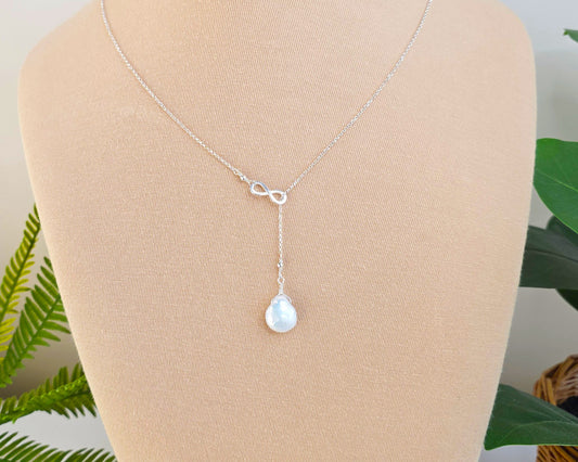 Large Pearl Drop Sterling Silver Infinity Lariat Necklace on beige display bust with plants in background 