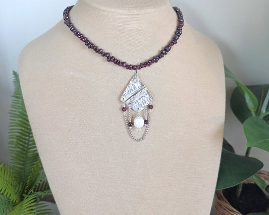 Deep Red stone beaded lariat style necklace with a Large Silver pendant with dangling stones white pearl and chains on beige  display bust and plants 