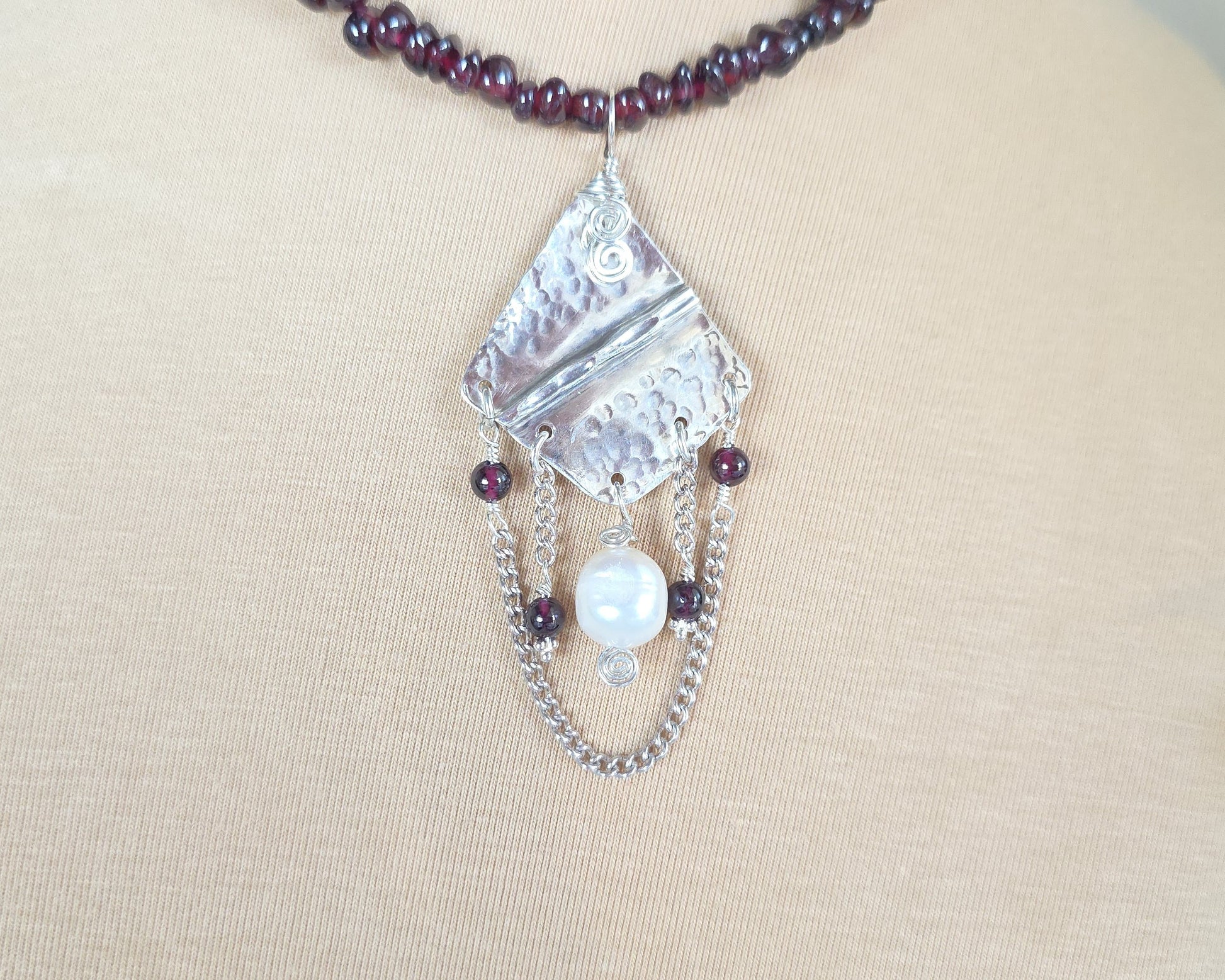 Deep Red stone beaded lariat style necklace with a Large Silver pendant with dangling stones white pearl and chains on beige display bust 