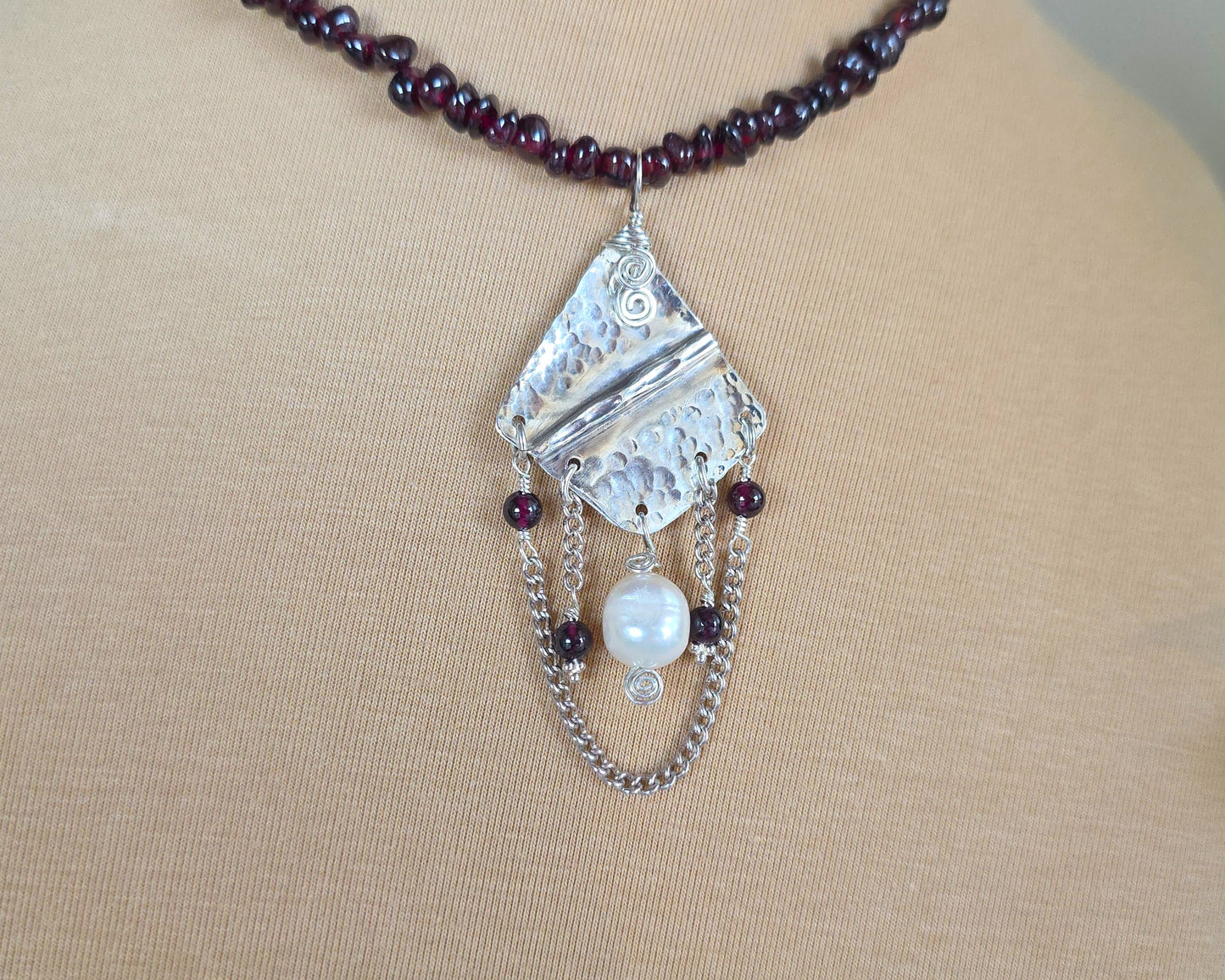 Deep Red stone beaded lariat style necklace with a Large Silver pendant with dangling stones white pearl and chains on beige  display bust and plants 
