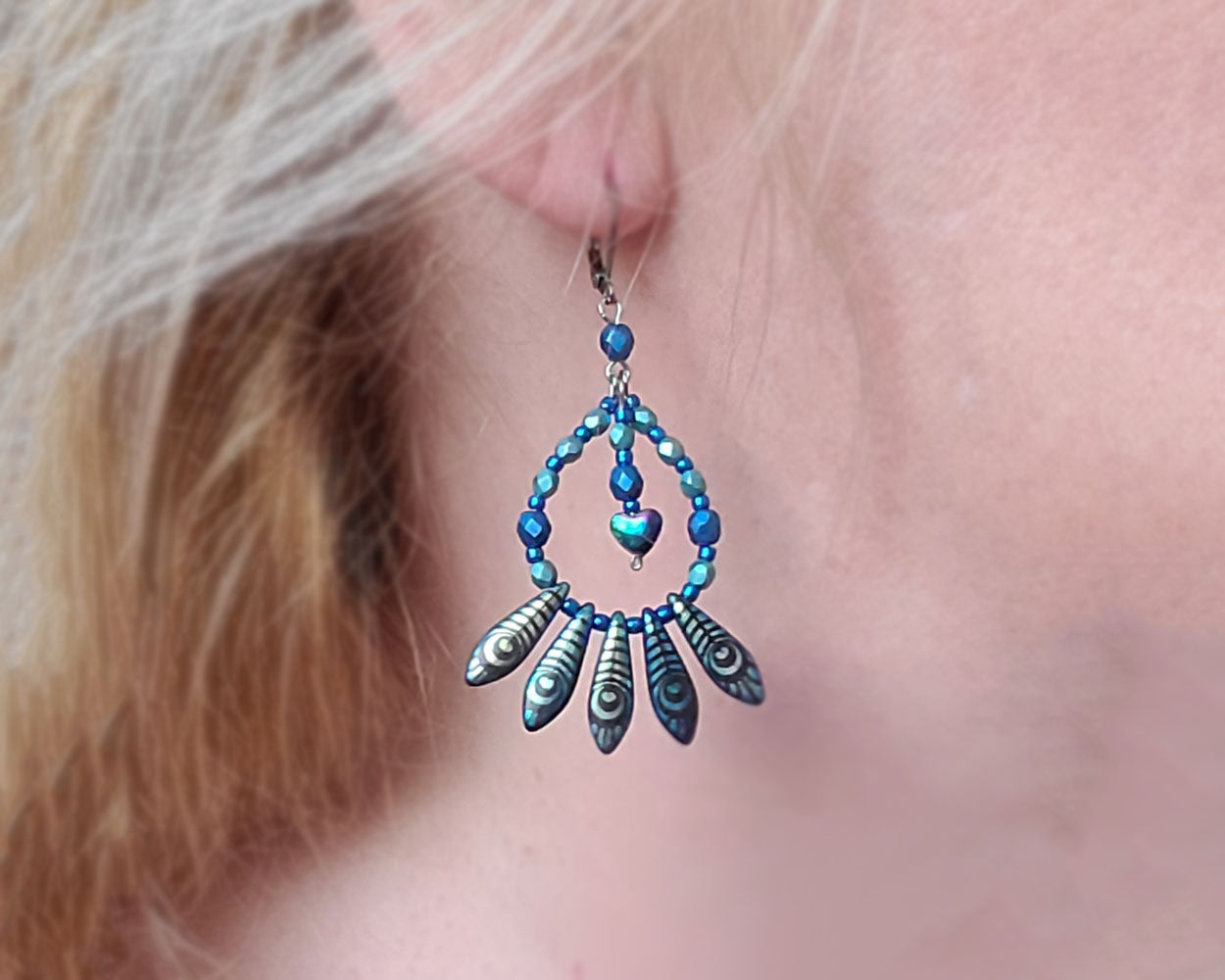 Long Dangling Hoop Fan Earrings with five peacock feather fanning the base of a drop shaped hoop made with stunning blue glass beads and a dangling titanium electroplated Hemalike heart. 