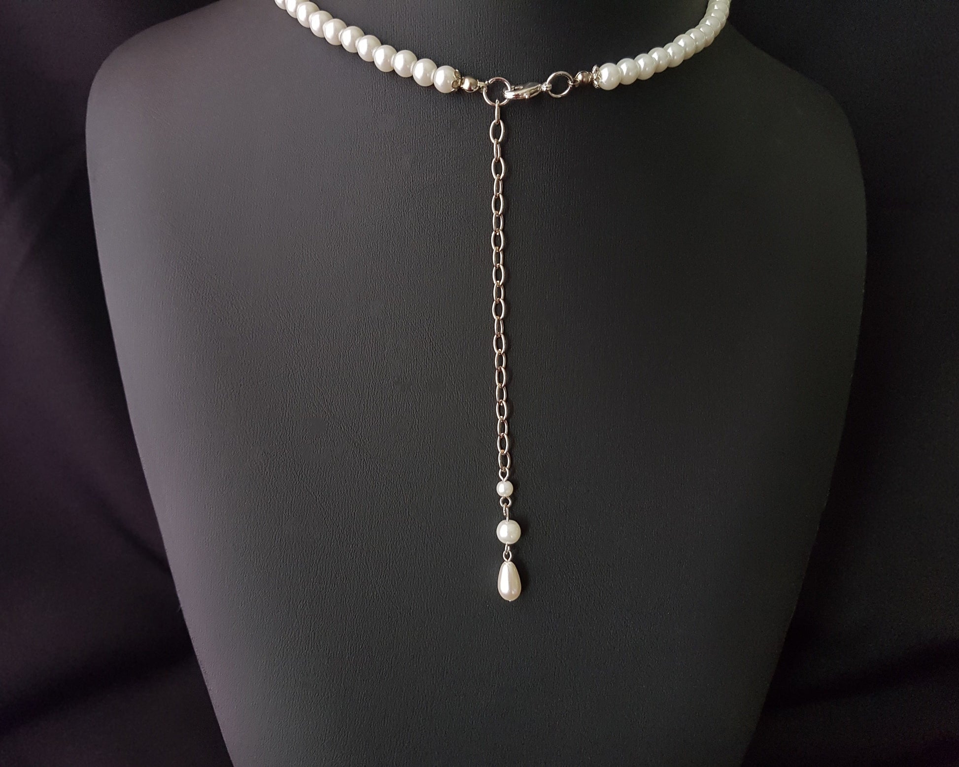  long back chain with another pearl drop displayed on black. 