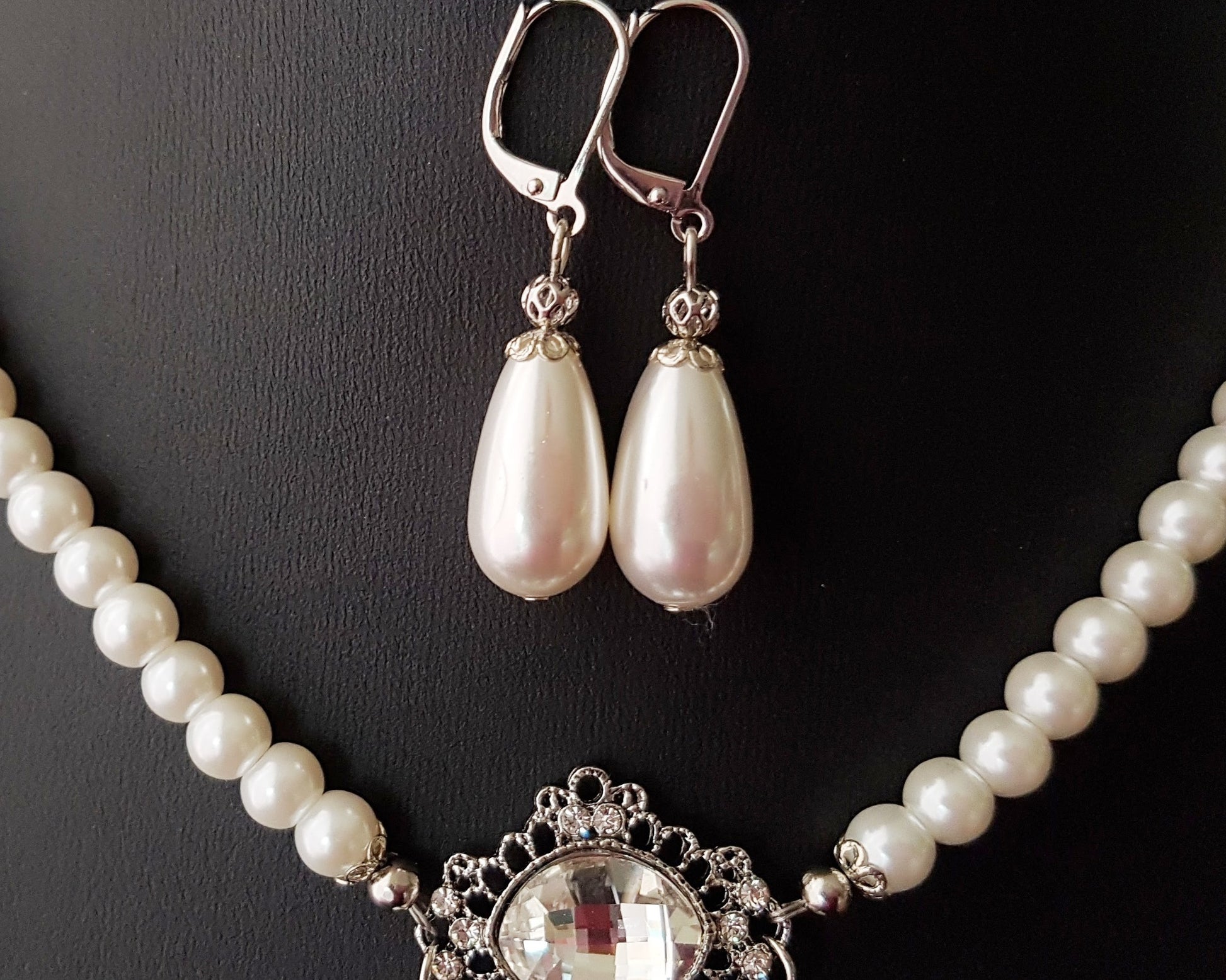 earrings are drop shaped pearls, displayed on black. 