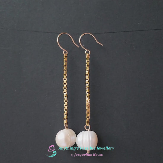 Video of a pair of extra long white pearl dangle earrings on long gold box chain with french earring hooks and black background 