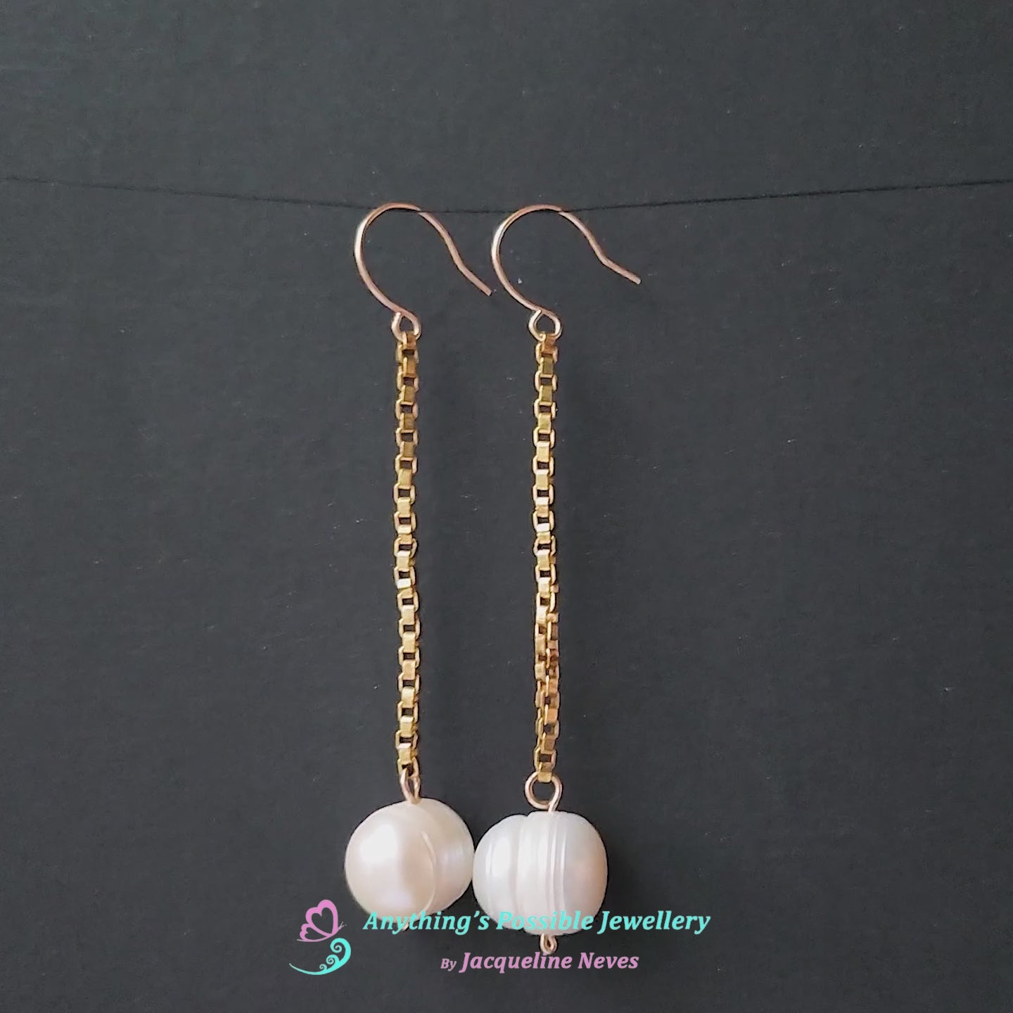 Video of a pair of extra long white pearl dangle earrings on long gold box chain with french earring hooks and black background 