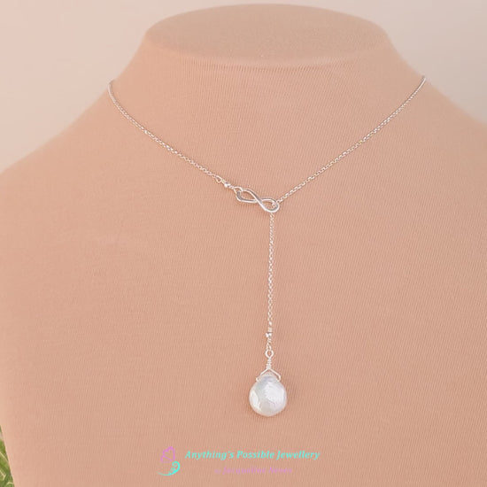 Video of a handmade large Pearl Drop Sterling Silver Infinity Lariat Necklace on beige display bust with plants in background 
