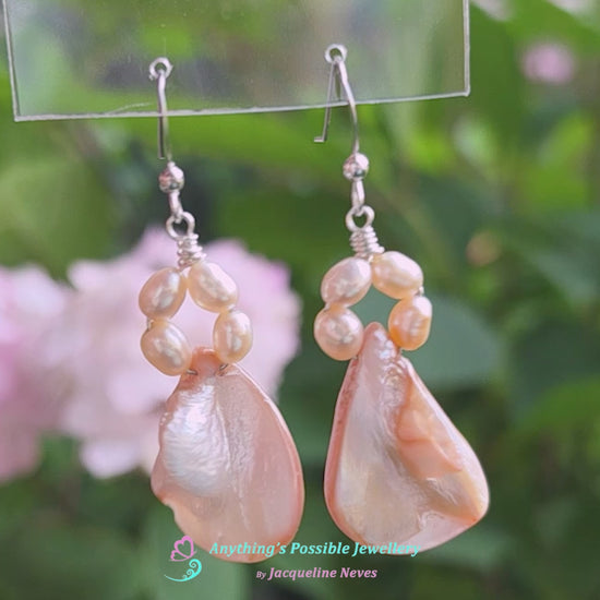 Video of A pair of Pale Pink Freshwater Cultured Peral and Vintage Shell Drop Earrings on Sterling Silver French earring hooks dangling in front of hand with garden in background.