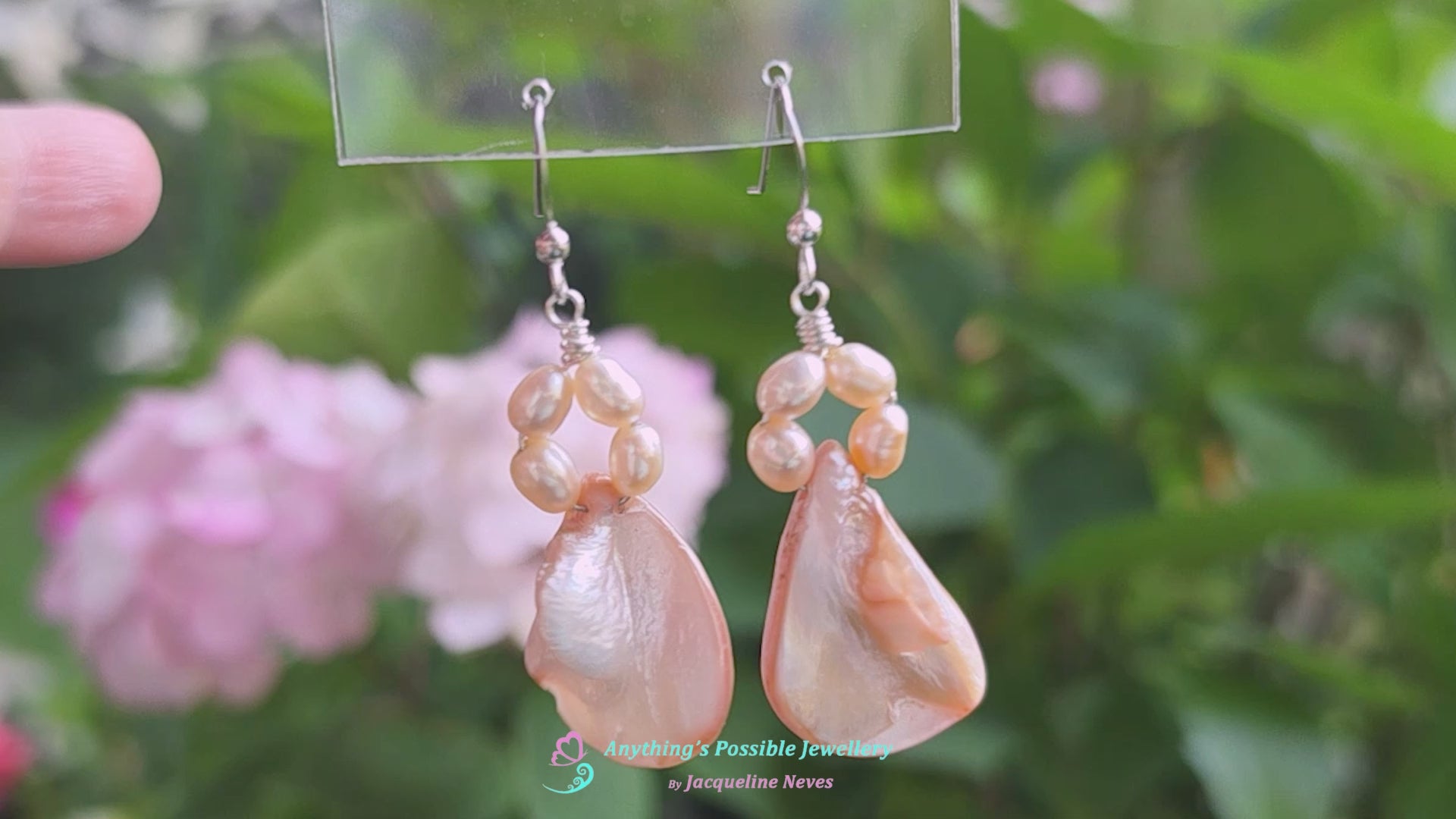 Video of A pair of Pale Pink Freshwater Cultured Peral and Vintage Shell Drop Earrings on Sterling Silver French earring hooks dangling in front of hand with garden in background.