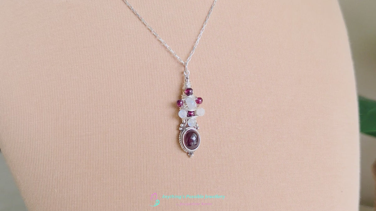 Vido of Handmade Boho style wire wrapped pendant with oval shape deep red Garnet gemstone wrapped with sterling silver wire small round garnets and faceted Moonstones on chain with beige cloth background 