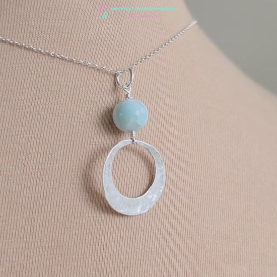 Video of a Handmade round sterling silver pendant with wire wrapped round pale blue larimar stone dangling on chain displayed on beige display bust
