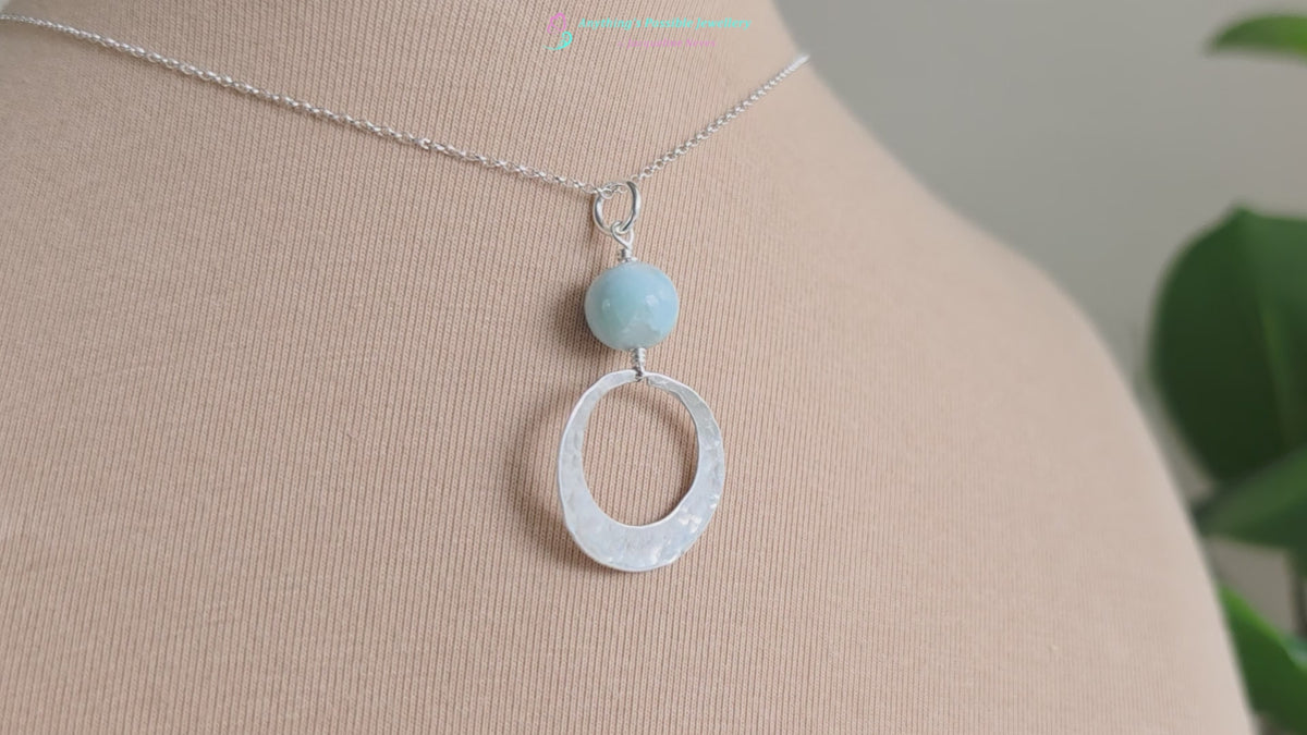 Video of a Handmade round sterling silver pendant with wire wrapped round pale blue larimar stone dangling on chain displayed on beige display bust