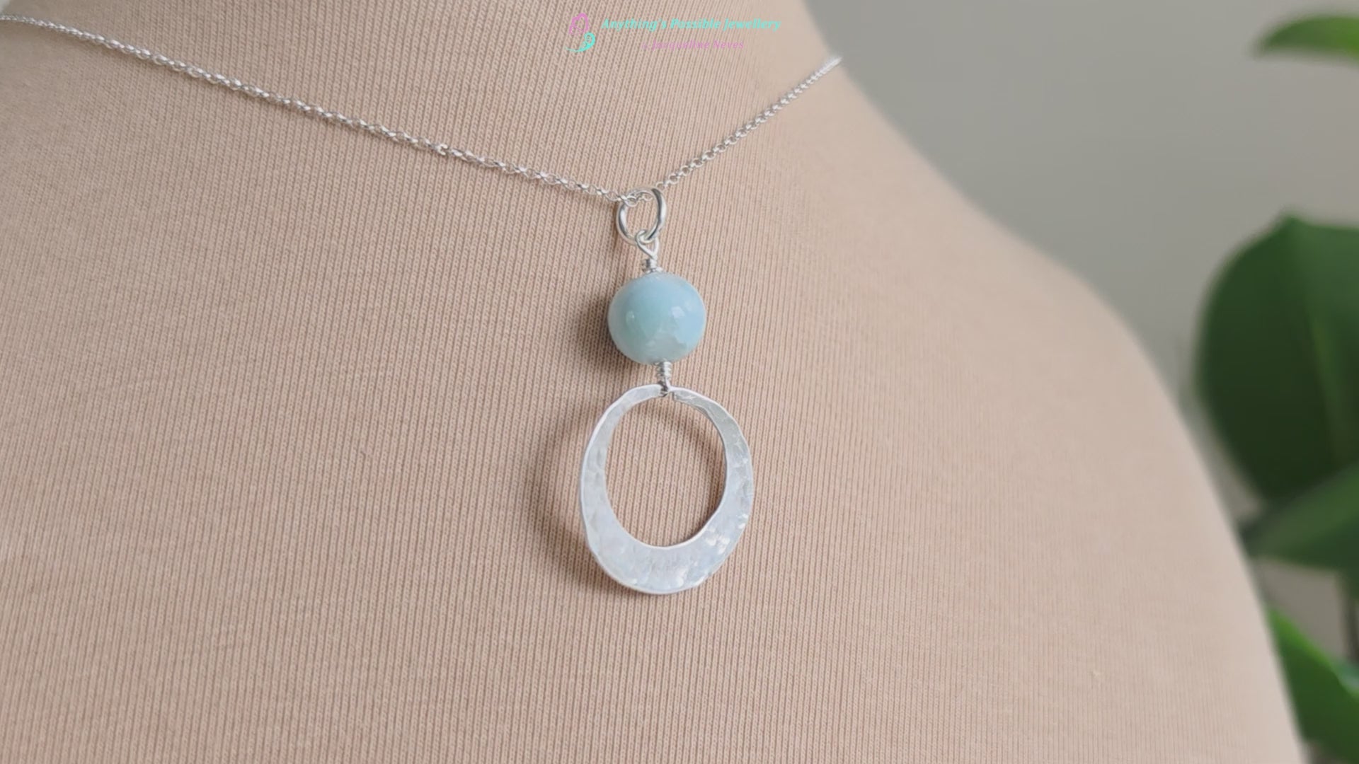 Video of a Handmade round sterling silver pendant with wire wrapped round pale blue larimar stone dangling on chain displayed on beige display bust