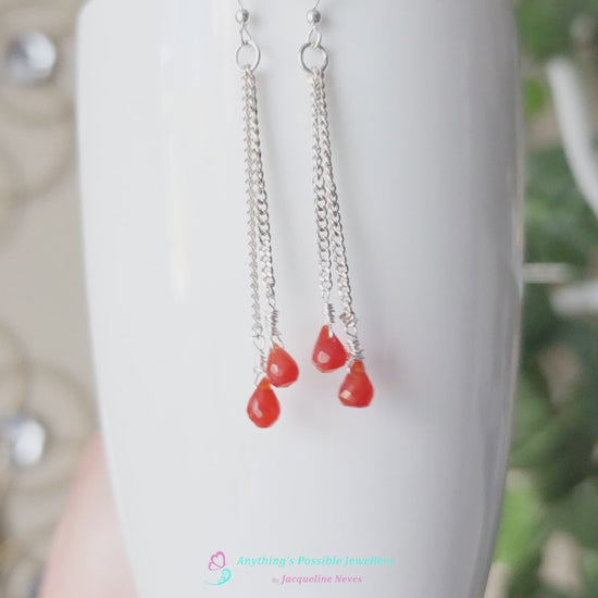 Video of a pair of handmade long dangle earrings with orange faceted Carnelian drop shaped stones dangling from Sterling Silver chain 